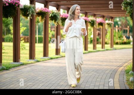 Gray-haired woman with coffee in blooming park Stock Photo