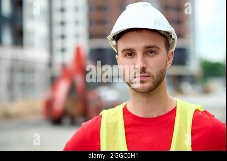 Serious serene young worker in a helmet staring ahead Stock Photo