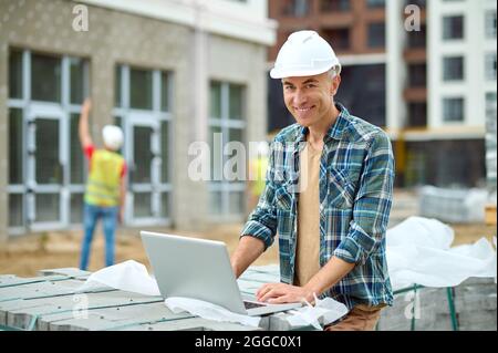 Joyous male working on his laptop on the building site Stock Photo