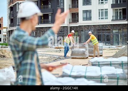 Two young builders looking at their colleague waving at them Stock Photo