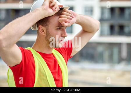 Exhausted male builder wiping sweat off his forehead Stock Photo