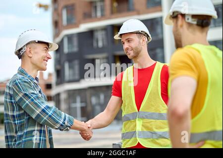 Handsome bearded Caucasian construction worker shaking his colleague hand Stock Photo