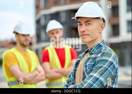 Three men in protective helmets standing on the building site Stock Photo