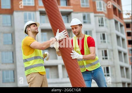 Experienced Caucasian workers in hardhats installing a drainage system Stock Photo