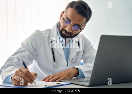 Indian male doctor in clinic working remotely using pc laptop computer. Stock Photo