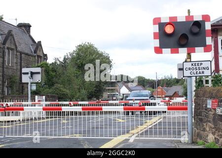 Railway level crossing barrier down with vehicles waiting for train to pass. Parbold, Lancashire, UK Stock Photo