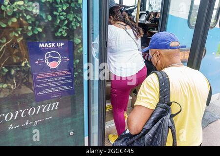 Miami Beach Florida free trolley public transportation wear wearing mask message Covid-19 health crisis pandemic coronavirus Hispanic man boarding Stock Photo