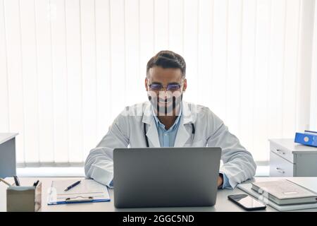 Indian happy male doctor in clinic consulting using pc laptop computer. Stock Photo
