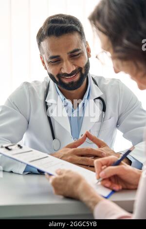 Smiling Indian doctor consulting female patient in clinic hospital. Vertical. Stock Photo