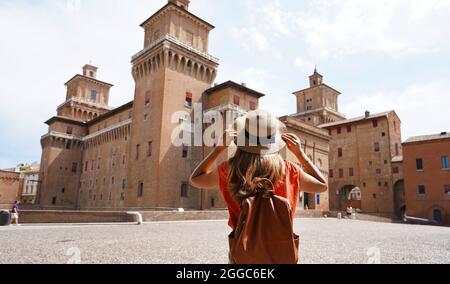 Travel in Italy. Back view of beautiful tourist girl enjoying view of Este Castle (Castello Estense) of Ferrara, Italy. Stock Photo