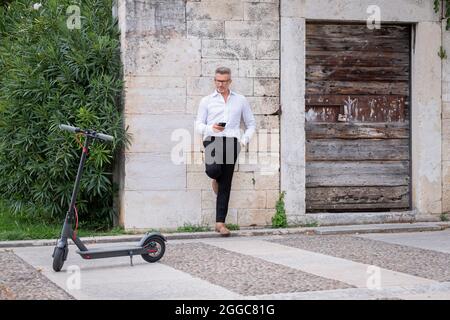 Young businessman using phone near electric scooter. Focus on scooter Stock Photo