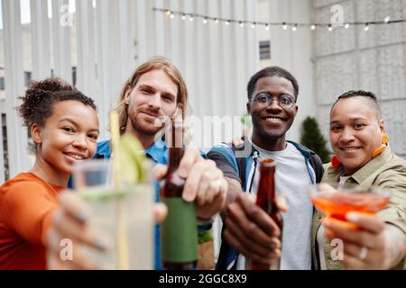 Diverse group of young people enjoying drinks at outdoor rooftop party and looking at camera Stock Photo
