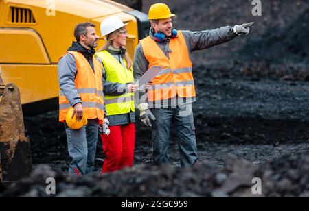 Three workers in quarry with heavy machinery Stock Photo