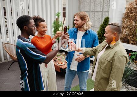 Diverse group of carefree young people clinking drinks while enjoying outdoor party with friends Stock Photo