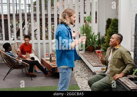 Side view portrait of smiling young man talking to friend while enjoying outdoor party at rooftop, copy space Stock Photo
