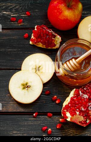 Traditional Jewish religious holiday Rosh Hashanah. Apples, pomegranates and honey on a dark wooden background. Vertical photo. Stock Photo