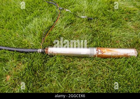 Faulty in ground lawn sprinkler pump lying in tall fescue grass in the process of being changed out for a new one. Stock Photo