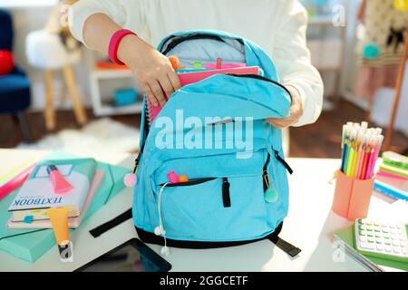 Closeup on child with workbooks and blue backpack packing for school at home in sunny day. Stock Photo