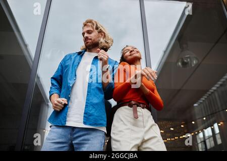 Low angle portrait of colorful young couple dancing at rooftop under sky, copy space Stock Photo