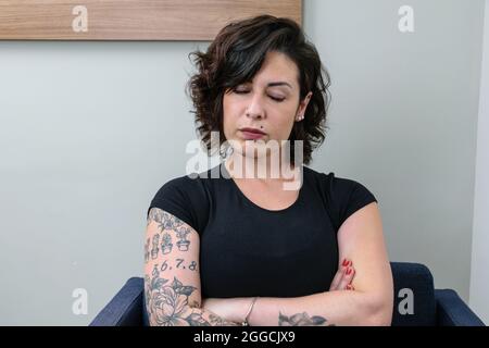 Brazilian woman, tattooed, with arms crossed and eyes closed. Upset and angry. Stock Photo