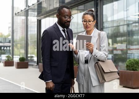 Two elegant multiracial colleagues preparing presentation in urban environment Stock Photo