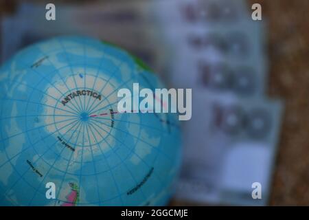Earth globe map of Antarctica, sitting on group of banknotes in nature. Stock Photo