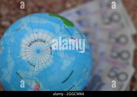 Earth globe map of Antarctica, sitting on group of banknotes in nature. Stock Photo