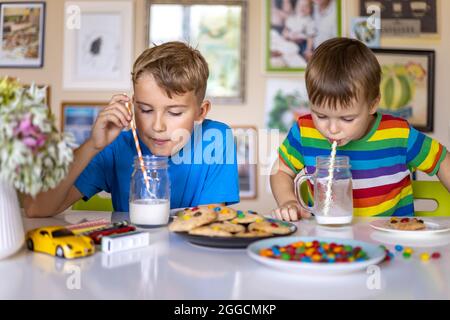Funny male brothers eat cookies with round multi-colored sweets m&m and drink milk. Stock Photo