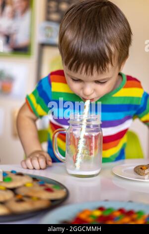 Funny boy eat cookies with round multi-colored sweets m&m and drink milk. Stock Photo