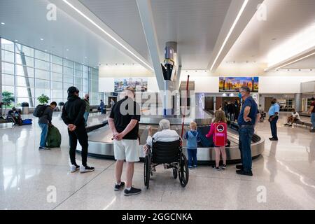 A handicapped woman waits in her wheelchair for her luggage alongside other travelers at the Indianapolis International Airport Baggage Claim in Indy. Stock Photo