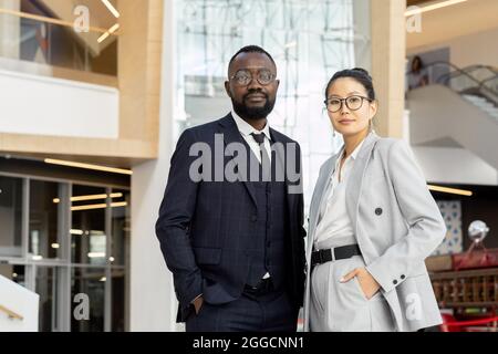 Two young elegant employees in suits standing inside large contemporary business center Stock Photo