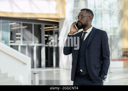 Young elegant businessman communicating on mobile phone while standing in contemporary business center Stock Photo
