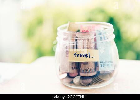 Saving money for travel jar concept. Money box on empty table collect banknote and coins for holiday trip budget. Stock Photo