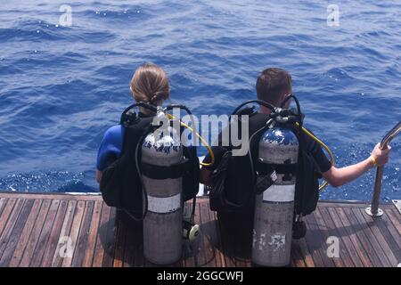 a man and a woman with scuba gear in diving suits are preparing to dive into the water.  Stock Photo