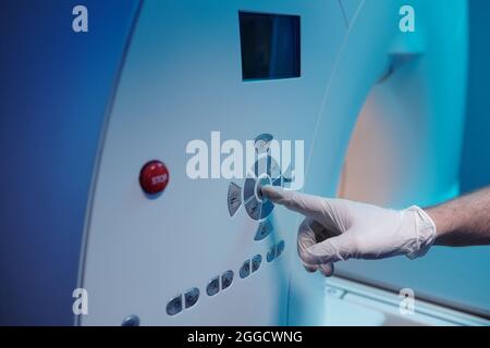 Gloved hand of radiographer pressing start button on panel of mri scan machine Stock Photo