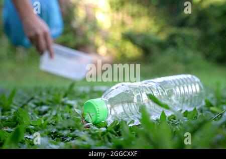 Plastic bottle with volunteer at the background picking up plastic rubbish. Volunteering and plastic pollution concept. Stock Photo