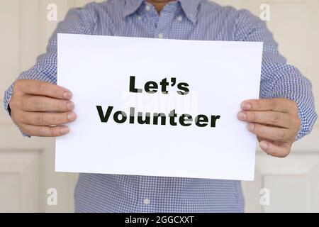 Man holding a piece of white paper with words, Lets Volunteer. Stock Photo