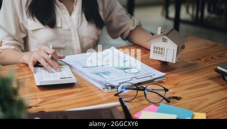businesswoman with house model doing finances and calculate about cost to real estate investment and in other, tax system. Business Financing Stock Photo
