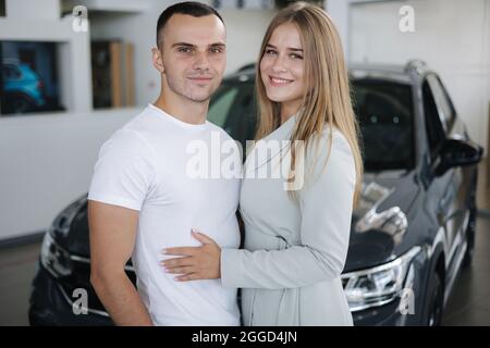 Portrait of beautiful young couple happy after buying new car from car showroom. Woman hus her man and glad Stock Photo