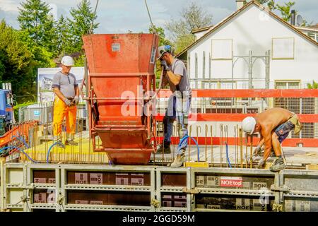 Builders pour concrete into the formwork of the wall. Apartment building construction project in Riehen, Basel, Switzerland. Stock Photo