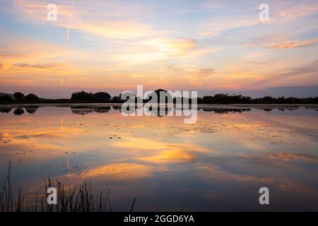 Beautiful bright colored sunset lit sky with orange clouds with reflection in lake water. Broad pond, Gower Peninsula, Wales, United Kingdom. Stunning sunset landscape. Stock Photo