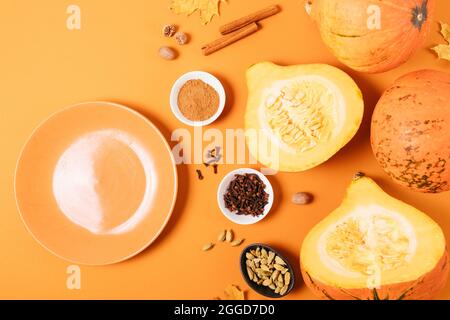 Empty plate next to pumpkins, spices and autumn leaves on orange background, flat lay. Stock Photo