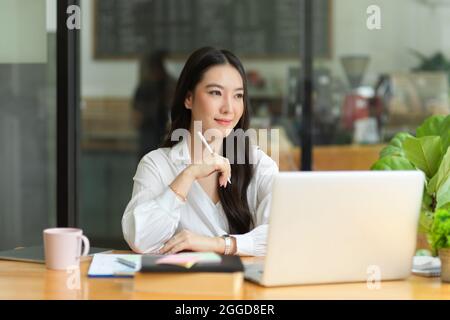Confident young businesswoman thinking about work, sitting at coffee shop Stock Photo