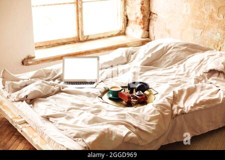 Work from home, the rays of the morning sun, and random things scattered on the bed. A laptop, retro camera, a cup of coffee, wireless headphones, a m Stock Photo