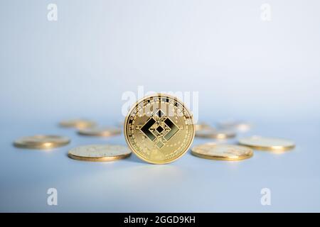 Binance BNB cryptocurrency coin standing centrally placed among bunch of crypto gold coins on blue background. Close-up, soft focus. Stock Photo