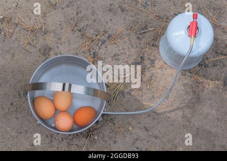 Traveler foods for outdoor activities. Eggs in pot in the green forest. Camping food making. Stock Photo