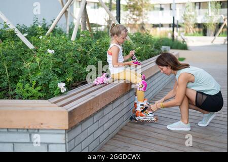 Caucasian woman helping her daughter put on roller skates. Stock Photo