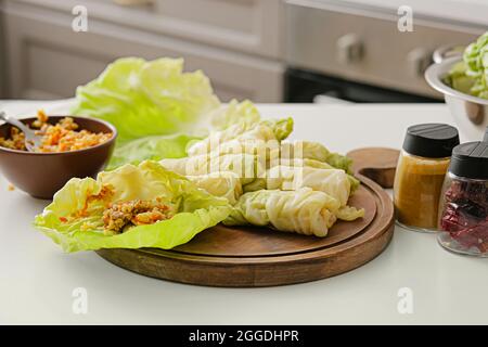 Wooden board with raw stuffed cabbage rolls and ingredients on table in kitchen Stock Photo