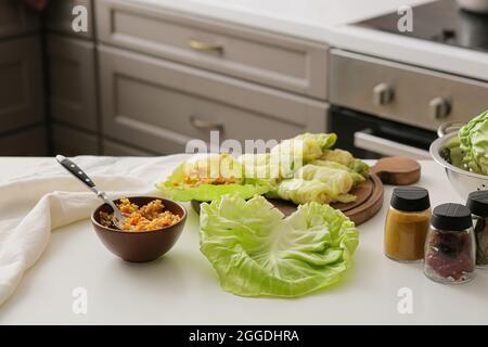 Wooden board with raw stuffed cabbage rolls and ingredients on table in kitchen Stock Photo