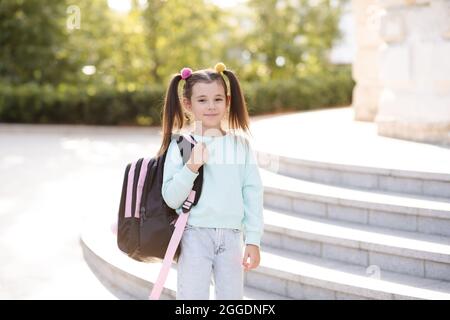 Smiling sweet happy little kid girl 5-6 year old wear casual clothes and backpack. Pupil child prepare for studying. Back to school. Autumn season. Ha Stock Photo